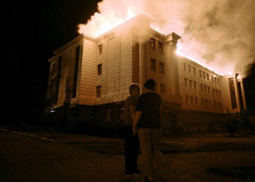 Прохожие смотрят на огонь, сжигающий школу в центре Донецка 27 августа 2014 года, после попадания снаряда украинской армии. Несколько мирных жителей погибли в этот же день, когда их автомобиль был полностью сожжен прямым попаданием снаряда в центре Донецка.
