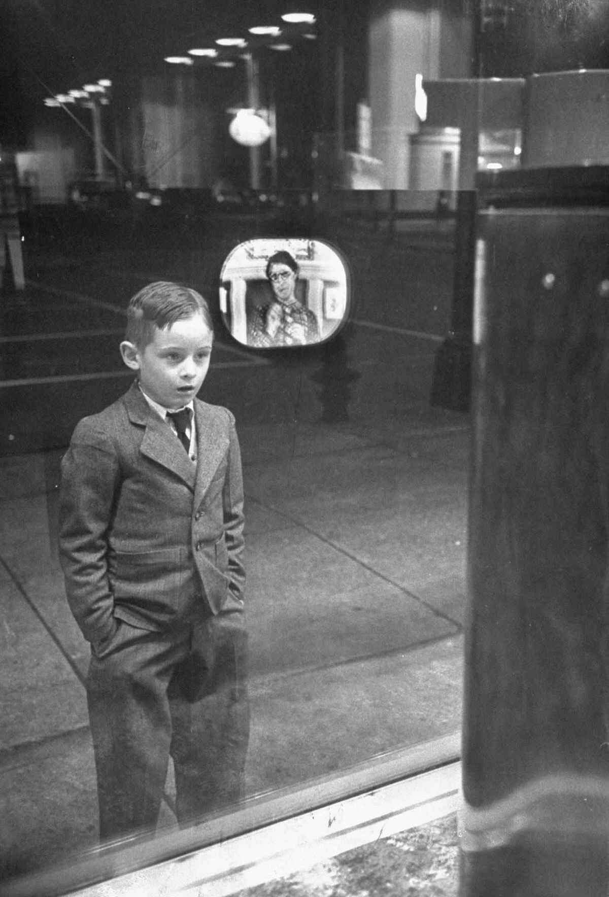 Мальчик стоит перед витриной магазина, где продаются первые телевизоры