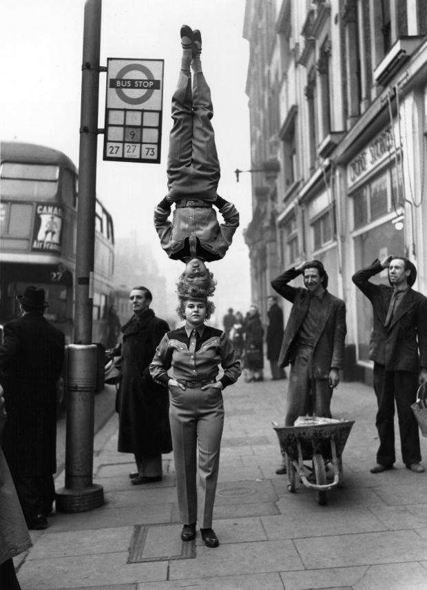 Прохожие смотрят на двоих циркачей на Hammersmith Broadway в Лондоне