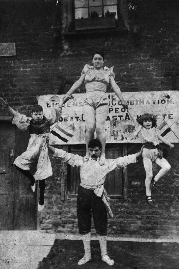 Уличный артист балансирует с женщина и двумя детьми в 1890 году