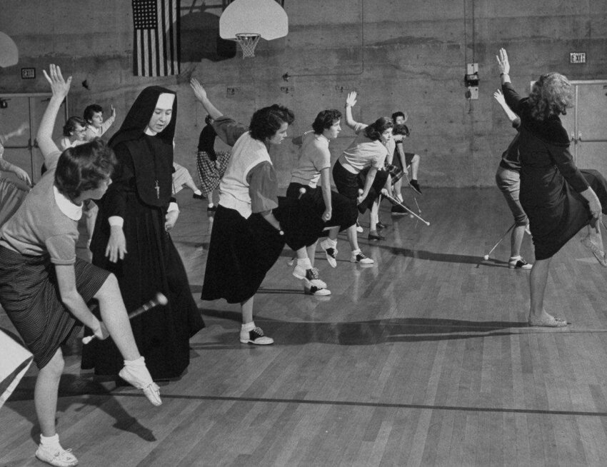 A group of girls from Parochial High School's Pep Club practicing with batons in the gym while the sister nun is coaching them on. (Photo by Nat Farbman/The LIFE Picture Collection/Getty Images)