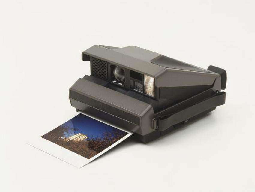 Polaroid camera with photographic print ejected from paper slot, close up