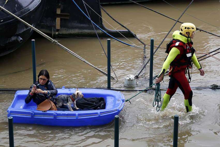 A fireman pulls a woman and her dog to shore, by a row of houseboats on the river Seine in Paris France, Wednesday June 1, 2016. The Seine River has overflowed embankments in Paris as floods hit or threaten cities and towns around France.(AP Photo/Jerome Delay)