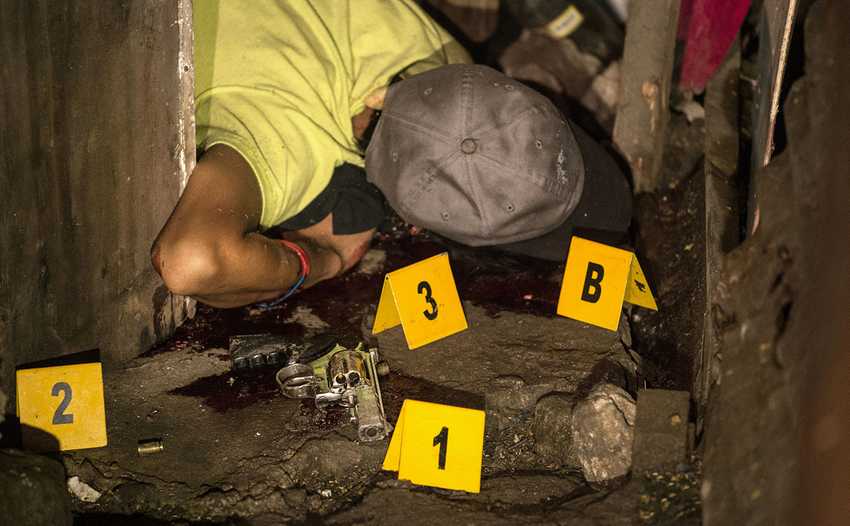 EDITORS NOTE: Graphic content / A suspected drug pusher lies dead on the ground as a police crime scene operative gathers forensic evidence after three suspected drug pushers were killed when a drug bust operation ended in a shootout with authorities in Manila early on June 25, 2016. Catholic Church leaders in the Philippines expressed alarm June 20 at a sharp rise in police killings of suspected criminals since the election of a firebrand president who has vowed a bloody war on crime. Their condemnation flies in the face of Philippine president-elect Rodrigo Duterte's call to police and even civilians to kill drug criminals. / AFP / NOEL CELIS / GRAPHIC CONTENT (Photo credit should read NOEL CELIS/AFP/Getty Images)
